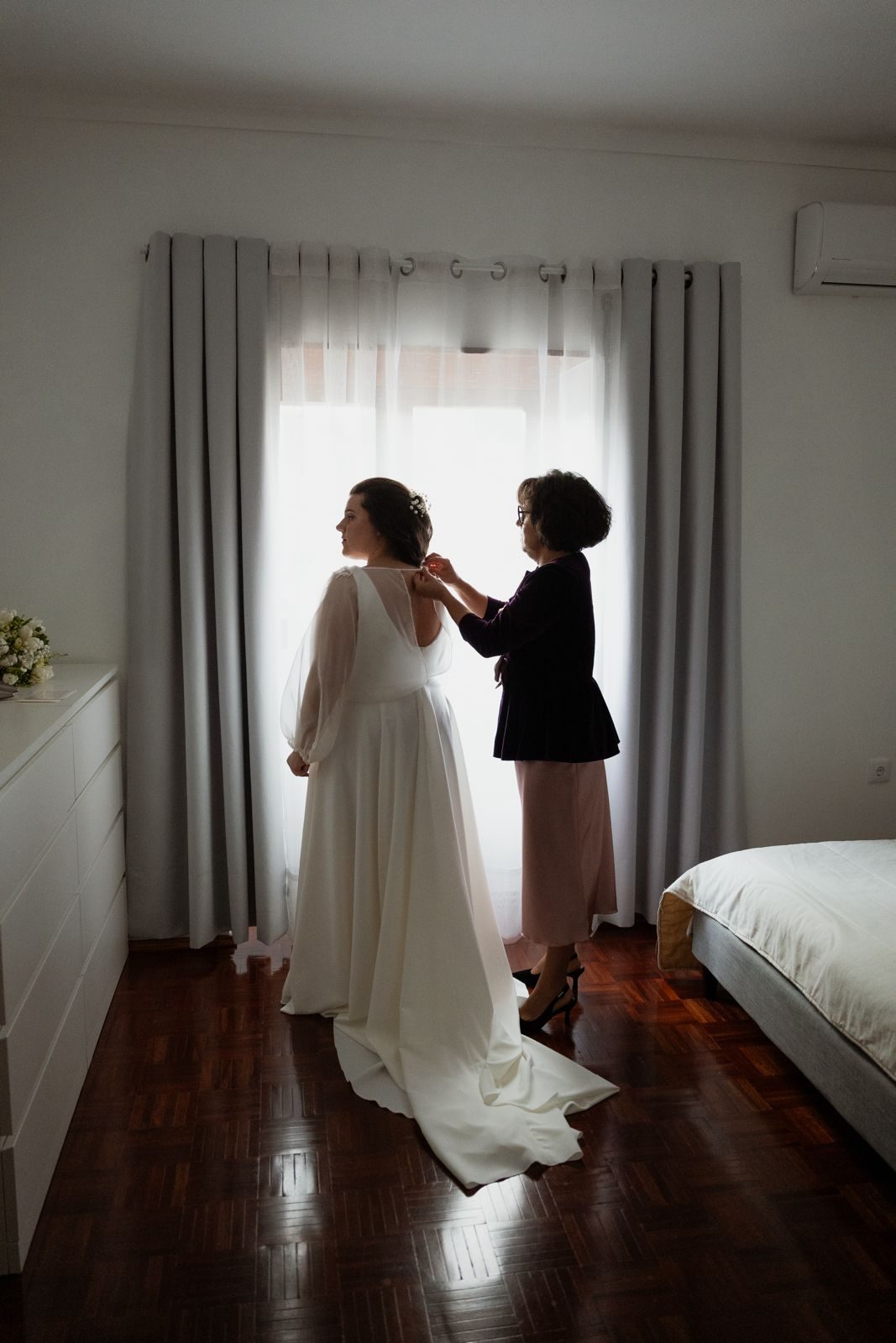 Noiva a vestir o vestido junto à janela